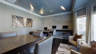This business center combines functionality with contemporary design across a single thoughtfully arranged floor. The space features a striking stacked-stone accent wall that serves as the backdrop for multiple computer workstations, each equipped with monitors and built-in desk surfaces, providing dedicated areas for productivity. A dark-stained wood conference table anchors the room, surrounded by upholstered chairs with nailhead trim detailing, offering a refined space for meetings or collaborative work. The deep teal ceiling adds a bold architectural contrast to the soft grey walls, while recessed lighting ensures the space is evenly and warmly illuminated throughout. Dark hardwood flooring runs throughout the room, grounding the overall aesthetic and complementing the mix of textures found in the furnishings. A chevron-patterned area rug and a cream accent chair contribute to a lounge-like corner, balancing the professional atmosphere with comfort. Architectural wall art adds a visual focal point, enhancing the polished, urban character of the space.