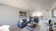 Located at 919 East Lemon Street in Tempe, Arizona, this two-bedroom, one-bathroom unit offers a well-organized single-floor layout that makes efficient use of its compact footprint. The living room serves as the heart of the home, characterized by painted brick walls, light wood-style flooring, and a textured ceiling. Natural light filters in through a front-facing window, creating a bright and welcoming atmosphere. The space flows directly into the kitchen, which features white cabinetry, a mosaic tile backsplash, stainless steel appliances including a gas range and full-size refrigerator, and a peninsula counter with bar seating — ideal for casual dining or entertaining. A hallway connects the main living areas to the two bedrooms and shared bathroom. Both bedrooms carry the same painted brick accent walls and wood-style flooring found throughout the unit, each benefiting from windows that bring in natural light and views of the surrounding greenery. The primary bedroom offers a comfortable amount of space for a bed and a dedicated study area. The shared full bathroom is clean and functional, featuring a tub-shower combination, a single vanity, and a toilet. The overall aesthetic is modern and casual, with a consistent palette of light grey tones and clean finishes throughout.