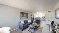Located at 919 East Lemon Street in Tempe, Arizona, this two-bedroom, one-bathroom unit offers a well-organized single-floor layout that makes efficient use of its compact footprint. The living room serves as the heart of the home, characterized by painted brick walls, light wood-style flooring, and a textured ceiling. Natural light filters in through a front-facing window, creating a bright and welcoming atmosphere. The space flows directly into the kitchen, which features white cabinetry, a mosaic tile backsplash, stainless steel appliances including a gas range and full-size refrigerator, and a peninsula counter with bar seating — ideal for casual dining or entertaining. A hallway connects the main living areas to the two bedrooms and shared bathroom. Both bedrooms carry the same painted brick accent walls and wood-style flooring found throughout the unit, each benefiting from windows that bring in natural light and views of the surrounding greenery. The primary bedroom offers a comfortable amount of space for a bed and a dedicated study area. The shared full bathroom is clean and functional, featuring a tub-shower combination, a single vanity, and a toilet. The overall aesthetic is modern and casual, with a consistent palette of light grey tones and clean finishes throughout.