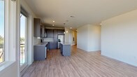 This single-floor unit showcases a contemporary design with a cohesive blend of modern finishes throughout. The open-concept kitchen and living area forms the heart of the space, where light wood-tone laminate flooring extends seamlessly across the main living zone. The kitchen is well-appointed with dark espresso cabinetry, granite countertops, stainless steel appliances including a refrigerator with ice maker, dishwasher, range, and microwave, alongside a central island that provides additional workspace and separates the kitchen from the expansive living area. Recessed lighting and pendant fixtures illuminate the space effectively.

The living area is generously proportioned with clean white walls and open sightlines that connect smoothly to the rest of the unit. The bedrooms feature plush neutral carpeting and large windows that frame outdoor views of surrounding greenery, allowing for ample natural light. Each room offers a calm, versatile atmosphere suitable for various uses.

The bathrooms are finished with large-format tile flooring, dark cabinetry with granite countertops, and well-sized mirrors. One bathroom includes a glass-enclosed shower, while another features a separate walk-in area with additional storage potential. Overall, the unit presents a clean, modern aesthetic with practical, quality finishes throughout.