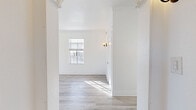 Located at 535 S Gramercy Place in Los Angeles' Koreatown neighborhood, this single-floor unit offers a thoughtfully laid-out living space with a bright, airy aesthetic throughout. Light hardwood-style flooring flows seamlessly across the living areas, complemented by crisp white walls, crown molding, and classic wall sconces that lend a warm, timeless character.

The living room is generously sized, featuring large multi-pane windows that invite abundant natural light and showcase classic architectural detailing, including decorative column trim at the entryway. A vintage cast-iron radiator adds a charming period touch. The space connects naturally through a hallway to the rest of the unit.

The kitchen is efficiently designed with modern white gloss cabinetry, dark countertops, and a full suite of stainless steel appliances including a gas range, microwave, and refrigerator. An arched ceiling detail above the cabinetry adds architectural interest, while tile flooring provides a practical finish.

The bathroom is clean and bright, featuring a full soaking tub with shower, pedestal sink, tile flooring, and a window for natural ventilation. Four closets throughout the unit provide exceptional storage. The dedicated entrance and hallway ensure a smooth and organized flow between all areas of the home.