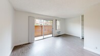 This single-floor unit in Canoga Park offers a efficiently designed open-concept layout. The main living area features light wood-style laminate flooring and a textured ceiling, creating a clean, neutral aesthetic throughout. A peninsula-style kitchen integrates seamlessly into the living space, outfitted with white cabinetry, a countertop range, refrigerator, and under-cabinet lighting, making the most of the compact footprint.

Natural light is a notable feature, with a wide sliding glass door dominating one wall of the living area and opening to a private patio enclosed by a wood fence. An additional window alongside the slider further brightens the space. A wall-mounted HVAC unit provides climate control directly in the living area.

The sleeping area is defined by light-toned walls, matching laminate flooring, built-in open shelving, and a closet, offering practical storage solutions. The bathroom includes a wide vanity with white cabinetry, a large mirror, and a shower/tub combination, maintaining the consistent white-and-neutral palette found throughout the unit. Overall, the space presents a bright, functional, and low-maintenance living environment.