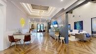 Located at 3535 SW 20th St in Ocala, Florida, this single-story leasing office is thoughtfully designed to create a welcoming and professional environment. The reception area greets visitors with striking herringbone-patterned hardwood flooring, an elegant tray ceiling with a statement chandelier, and a sleek white shiplap front desk accented by a glowing branded logo sign. Crown molding and recessed lighting add refined detail throughout.

The open layout flows seamlessly from the reception into a comfortable lounge area furnished with plush white sofas, curated artwork, and natural wood accent tables. Adjacent to the lounge, a glass-enclosed conference room provides a private meeting space equipped with a wall-mounted display, a live-edge wooden conference table, and leather executive chairs, all bathed in natural light from large windows with sheer drapery.

A dedicated refreshment bar features white shaker cabinetry, dark subway tile backsplash, stainless steel appliances, open wood shelving, and a mounted display screen — ideal for hosting guests. A secondary meeting area with a round wood table, leather chairs, and open shelving offers additional flexibility, with glass double doors opening to outdoor views. Exposed dark wood beams, shiplap accent walls, and abundant greenery complete the space's warm yet polished aesthetic.