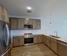 This 800-square-foot, fourth-floor apartment at 8020 Windrose Ave in Plano, Texas offers a well-appointed 1-bedroom, 2-bathroom layout with modern finishes throughout. Light wood-look flooring flows through the open-concept kitchen and living area, while the kitchen features warm-toned shaker cabinetry, granite countertops, a large center island with pendant lighting, subway tile backsplash, and a full suite of stainless steel appliances including a gas range, built-in microwave, and French door refrigerator. The combined kitchen and living area provides a seamless, functional layout ideal for everyday living. The 140-square-foot primary bedroom is carpeted and includes a ceiling fan and windows offering outdoor views. The primary bathroom is equipped with a dual-sink vanity, granite countertops, matching cabinetry, and a spacious walk-in shower. A second full bathroom features a single vanity with granite countertop and framed mirror. A dedicated laundry room includes washer/dryer hookups and a water heater. The unit also includes a closet for additional storage. Natural light is prominent throughout, with multiple windows framing outdoor views of the surrounding Plano landscape.