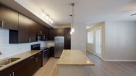 This single-floor residence is thoughtfully designed with a contemporary aesthetic and functional layout. The kitchen serves as a central highlight, showcasing rich dark-espresso cabinetry, granite countertops, and a full suite of stainless steel appliances, including a refrigerator, range, microwave, and dishwasher. A white subway tile backsplash adds a clean, modern contrast to the cabinetry, while a generously sized island with matching granite provides additional prep and seating space. Pendant lighting and a track light fixture illuminate the kitchen, enhancing its polished look.

The open-concept living and dining area features wood-style plank flooring, neutral-toned walls, and a ceiling fan with light kit. Multiple windows fitted with horizontal blinds allow natural light to fill the space, and a private entry door provides direct access. The bedroom areas are carpeted for comfort, with one bedroom featuring a walk-in closet equipped with built-in shelving. The bathroom includes a granite-topped vanity with an undermount sink, a large mirror, and a tub-shower combination with tile surround. Overall, the space presents a clean, move-in-ready environment with consistent finishes throughout.