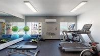 This single-floor fitness center is thoughtfully designed to support a comprehensive workout experience. The space is divided into distinct functional zones, each catering to different aspects of physical training. The cardio area is equipped with Matrix treadmills, stationary spin bikes, and a stair climber, all positioned near large windows that invite natural light and outdoor views, creating an energizing atmosphere during workouts. A wall-mounted flat-screen TV adds entertainment for those longer cardio sessions.

The strength training zone features a Matrix functional trainer cable machine with TRX suspension straps, kettlebells, and a well-stocked dumbbell rack, offering a wide range of resistance and functional movement exercises. Weightlifting benches are positioned throughout for versatility.

A dedicated stretching and flexibility area is stocked with exercise balls, foam rollers, resistance bands, and medicine balls neatly organized on racks. A large wall mirror spans one side of the room, enhancing the sense of space and allowing users to monitor their form. Motivational typography wall art adds an encouraging ambiance throughout.

The facility features rubber flooring for safety and durability, recessed panel lighting, and a wall-mounted mini-split HVAC system ensuring year-round comfort. Glass-panel doors connect to an adjacent room, adding to the open, accessible layout of this well-appointed fitness space.
