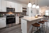 Located at 4215 Third Ave S in Birmingham, Alabama, this single-floor unit offers a well-designed layout with modern finishes throughout. The kitchen serves as a central highlight, featuring granite countertops, crisp white cabinetry, stainless steel appliances including a range, built-in microwave, dishwasher, and refrigerator, along with a textured tile backsplash. Open wood shelving adds a functional, contemporary touch. A central island with pendant lighting provides additional workspace and casual seating, making the kitchen ideal for both cooking and entertaining. The living area is bright and welcoming, benefiting from natural light through large windows that overlook outdoor greenery. Wood-style flooring runs through the main living spaces, contributing to a clean, cohesive aesthetic. The bedroom is generously sized with carpeted flooring, ample natural light, and direct access to both a private bathroom and a walk-in closet. The bathroom is finished with granite countertops, white cabinetry, a framed mirror, and contemporary light fixtures, maintaining the consistent modern style found throughout the unit. The overall ambiance is contemporary and well-appointed, with neutral tones and quality finishes creating a comfortable, functional living environment.