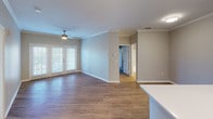 This single-floor residence offers a thoughtfully designed open-concept layout that seamlessly connects the kitchen and living areas. The kitchen is a standout feature, equipped with a full suite of stainless steel appliances including a refrigerator, range, microwave, and dishwasher. Crisp white shaker-style cabinetry lines both walls of the galley-style cooking zone, complemented by light quartz countertops and a peninsula with an undermount sink — ideal for both meal preparation and casual dining. Warm-toned wood-look flooring flows throughout the main living areas, enhancing the bright and airy feel of the space. Crown molding adds an elegant touch to the living room, which opens to a private outdoor area through French doors and is fitted with a ceiling fan overhead. The bedrooms are carpeted for comfort, each featuring natural light from slatted-blind windows and ceiling fans. Closet access and proximity to bathrooms make the secondary bedrooms equally functional. The bathrooms are clean and practical, each offering a full soaking tub and shower combination with white tile surround and chrome fixtures. Overall, the residence presents a neutral, modern palette with consistent finishes throughout, providing a comfortable and versatile living environment.