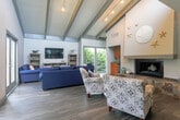 Located at 300 Glenwood Circle in Monterey, California, this single-floor community amenity space offers a thoughtfully designed layout that blends comfort and functionality. The living room is a standout area, showcasing soaring vaulted ceilings with exposed painted beams, rich hardwood-style flooring, and a striking stone-surround fireplace adorned with coastal-inspired décor including starfish and sand dollar accents. Plush blue sofas and patterned accent chairs create an inviting gathering atmosphere, complemented by a built-in media console and a convenient wet bar kitchenette. Large windows and sliding glass doors flood the space with natural light and provide outdoor access. The adjacent dining area features high-top tables and ladder-back chairs, with large windows offering views of the surrounding stairwell structure, accented by decorative wall clocks and nautical touches like a wooden anchor. The exercise room is a vibrant, well-equipped fitness center with bold teal and yellow accents, full-wall mirrors, and a comprehensive selection of cardio and strength-training equipment, including treadmills, cable machines, and stationary bikes. A connecting hallway and staircase provide seamless circulation throughout, making this a versatile and welcoming community hub in the heart of Monterey.