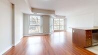 This thoughtfully designed 1-bedroom, 1-bathroom unit offers an efficient and comfortable single-floor layout. The open-concept living room is a standout feature, showcasing rich, warm-toned hardwood flooring that flows throughout, complemented by large windows that flood the space with natural light and offer views of the surrounding urban landscape. A raised ceiling detail adds architectural character to the living area.

The kitchen is well-equipped with warm-toned wood cabinetry, granite countertops, a double stainless steel sink, and a stainless steel appliance package. Tile flooring in the kitchen provides a practical transition from the hardwood in the living areas.

The bedroom is a comfortable, well-proportioned retreat featuring wood-tone laminate flooring, neutral walls, and a dedicated closet for storage. A window allows natural light to brighten the room.

The hallway connects the spaces efficiently, with tile flooring that ties into the entryway. The bathroom features a full soaker tub with a tiled surround accented by a decorative border, offering a clean and classic finish.

Overall, the unit presents a bright, neutral palette with consistent hardwood and tile flooring, creating a cohesive and inviting atmosphere throughout.
