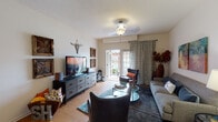 This single-floor apartment at Springhouse Apartments offers a thoughtfully designed layout with a comfortable flow between living, dining, and kitchen spaces. The living room features wood-look flooring, a ceiling fan with light fixture, and a sliding glass door that opens to a private outdoor balcony, filling the space with natural light and outdoor views. The kitchen is equipped with dark espresso cabinetry, granite countertops, stainless steel appliances including a microwave and range, and a breakfast bar that connects seamlessly to the adjacent dining area. The dining space accommodates a round table and is accented by a round wall mirror and contemporary artwork. Two well-sized bedrooms offer plush carpeting, large windows with blinds and drape panels that invite natural light, and ceiling fans for added comfort. The full bathroom includes a tiled tub and shower surround, a vanity with granite countertops, dark wood cabinetry, and a large mirror. A dedicated in-unit laundry room houses a full-size top-loading washer and dryer with overhead wire shelving for additional storage. Throughout the apartment, neutral tones and warm accents create a welcoming and cohesive ambiance.