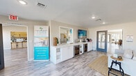 The Tides at Green Valley Apartments community clubhouse is a thoughtfully designed, single-floor facility that serves as the social and administrative hub of the property. The leasing office greets visitors with a sleek white shiplap reception counter, wood-style plank flooring, and recessed lighting throughout. A beverage station with dual wine coolers and a mirror-backed credenza adds a welcoming, hospitality-inspired touch to the front area.

Beyond reception, the space opens into a bright lounge area distinguished by soaring vaulted ceilings and an abundance of natural light. Wood-style flooring continues throughout, and coastal-themed artwork reinforces the community's identity. French doors lead to a sunlit seating area lined with large grid-pane windows overlooking the outdoor pool, furnished with high-top tables and bar stools for casual gatherings.

The community kitchen features crisp white cabinetry, subway tile backsplash, stainless steel appliances, and a generous quartz-topped island with bar seating — ideal for resident events. The fitness center is well-equipped with cardio machines, cable equipment, air bikes, and TRX systems, all set on vibrant multi-colored interlocking floor tiles, with mirrored walls and pool-facing windows enhancing the open, energetic atmosphere.