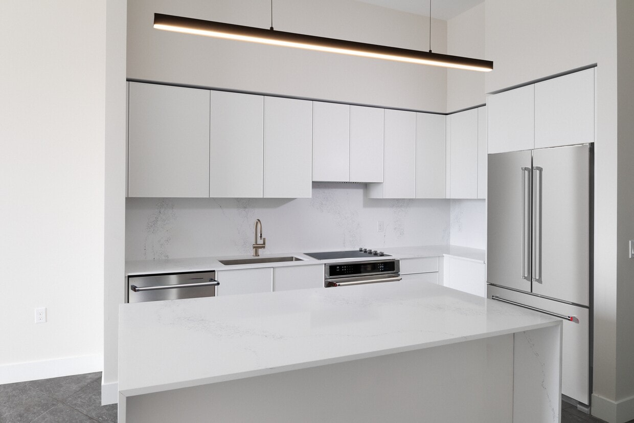 Colección Signature Cocina de apartamento de tres habitaciones con gabinetes blancos, encimera y protector contra salpicaduras de cuarzo de mármol blanco y electrodomésticos de acero inoxidable renovados. - Avalon South Miami