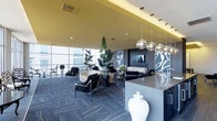 This stylish clubroom delivers a striking contemporary aesthetic through a carefully curated blend of contrasting tones and textures. The space is anchored by a bold color palette combining deep charcoal, warm gold-yellow ceiling accents, and crisp white elements that together create a dramatic yet inviting atmosphere. Floor-to-ceiling windows along one wall flood the interior with natural light while framing sweeping city views, enhancing the sense of openness and scale. Overhead, a series of polished chrome globe pendant lights serve as eye-catching focal points, casting warm ambient light across the room. The lounge area features sleek black furniture arrangements set atop patterned herringbone carpet in cool grey tones, providing comfortable seating throughout. A large flat-screen TV is mounted against a textured feature wall adorned with a bold botanical silhouette pattern in dark tones, adding artistic depth. Lush tropical plants positioned throughout the space introduce organic warmth against the modern décor. A countertop station in the foreground, accented with a decorative white ceramic jar, suggests a service or welcome area, completing the polished, hospitality-inspired design of this communal space.