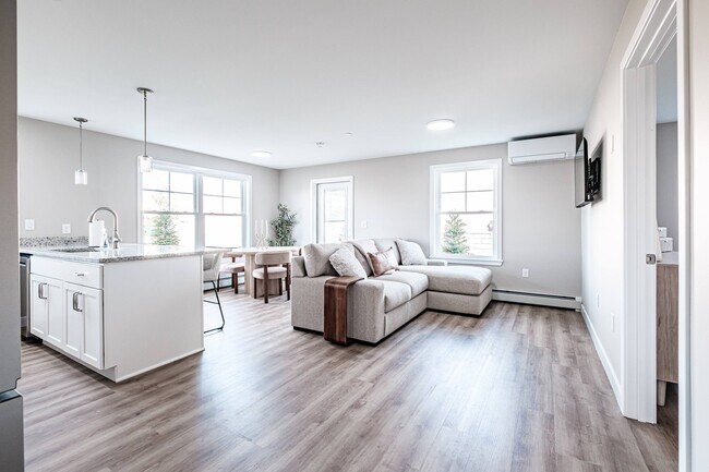 Disfrute de un espacio luminoso y diáfano con una perfecta integración entre la cocina, el comedor y la sala de estar, realzado por la abundante luz natural y los acabados modernos. - Windham Village Apartments