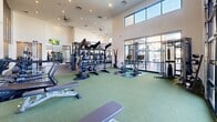 Located at 31925 N 29th Ave in Phoenix, AZ, this expansive fitness center is a single-floor exercise facility designed to deliver a full-scale gym experience. The space is defined by its dramatic soaring ceilings and floor-to-ceiling glass garage doors that flood the interior with natural light while offering outdoor views, creating an open and energizing atmosphere.

The facility is divided into distinct functional zones. The strength training area features a robust selection of cable machines, Smith machines, weight racks, and benches, all set against large wall mirrors that amplify the sense of space. Bold "PUSH" and "PULL" graphics in gold and gray adorn the walls, reinforcing the workout-focused ambiance. A dedicated functional training zone with turf flooring houses kettlebells, medicine balls, stability equipment, rowing machines, and battle ropes, providing ample space for dynamic and high-intensity workouts.

The cardio section is lined with a row of treadmills and stair climbers positioned beneath wall-mounted TVs, making for an engaging workout experience. Recessed lighting and ceiling fans throughout ensure comfort, while the light, neutral color palette keeps the environment bright and modern. The overall design is clean, purposeful, and well-organized, making this fitness center a standout amenity for the Phoenix community it serves.