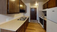 Located at 1223 Oak Hill Ct in Toledo, Ohio, this single-floor unit offers a practical and comfortable layout across several well-defined living spaces. The kitchen is equipped with dark wood cabinetry providing ample storage, a double-basin stainless steel sink, laminate countertops, a white electric range, and hardwood-style flooring that adds warmth to the space. A ceiling fan and direct access to an entry door make the kitchen both functional and convenient. The living area is generously sized, featuring wall-to-wall carpet, a baseboard heating unit, and a window air conditioning unit. Large vertical-blind-covered sliding doors allow abundant natural light to fill the room. An additional carpeted room, likely a bedroom, mirrors this setup with a bright window, baseboard heat, and neutral wall tones that create a calm atmosphere. The bathroom is cleanly finished with a full tub-shower combination, a toilet, wood-toned vanity with a white countertop sink, and a lighted medicine cabinet above. Wood-look flooring in the bathroom adds a cohesive, updated touch. Throughout the unit, neutral color palettes and practical finishes provide a clean, move-in-ready environment.