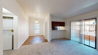 This single-floor residence offers a thoughtfully designed layout that balances comfort and functionality throughout. The open-plan living and dining area is bright and welcoming, featuring a combination of plush carpet and hardwood-style flooring. A pendant light fixture highlights the dining space, while a sliding glass door floods the living area with natural light and provides access to an outdoor patio. A half-wall with rich dark cabinetry above connects the living space to the kitchen, creating an open pass-through feel. The galley-style kitchen is well-equipped, showcasing dark espresso cabinetry, granite countertops, black appliances including a refrigerator and electric range, and hardwood-style flooring. A narrow window above the counter brings in additional natural light. The two bedrooms are carpeted and generously sized, each featuring windows with blinds. One bedroom includes a walk-in closet area, adding practical storage. The bathrooms are finished with dark wood vanity cabinetry, granite countertops, and hardwood-style tile flooring, lending a cohesive and polished aesthetic. Clean white walls and neutral tones throughout the residence create a bright, move-in-ready atmosphere.