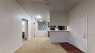 This single-floor residence is designed with a practical, open-concept layout that connects the main living area directly to the kitchen. The living space features neutral beige carpeting throughout, creating a cohesive and comfortable feel. Natural light filters in through windows fitted with horizontal blinds, while overhead lighting ensures the space remains well-lit. The entry door opens into the main living area, providing a straightforward and functional flow.

The kitchen is a standout feature, outfitted with dark wood cabinetry, white subway tile backsplash, and marble-style countertops that extend to a peninsula breakfast bar. Black appliances, including a refrigerator, electric range, microwave, and dishwasher, complement the cabinetry. Track lighting overhead illuminates the kitchen workspace, and rich hardwood-style flooring grounds the room with warmth and contrast.

The two bedrooms are carpeted, each equipped with a ceiling fan with light fixture and a window offering outdoor views. The rooms are well-proportioned with neutral walls and textured ceilings throughout.

The bathroom features a tub-shower combination with white tile surround, a dark wood vanity with a marble-style countertop, a single sink, and hardwood-style flooring. A mirrored medicine cabinet and towel bar complete the space efficiently.