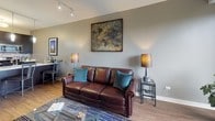 This single-floor residence offers a thoughtfully designed layout that balances comfort and functionality. The kitchen is outfitted with dark espresso cabinetry, stainless steel appliances including a French door refrigerator, gas range, and built-in microwave, complemented by a clean white countertop island and a blue mosaic tile backsplash. Warm hardwood-style flooring flows from the entry through the kitchen and into the living area.

The living room is generously proportioned, anchored by a sliding glass door that opens to a private balcony, filling the space with natural light and offering pleasant outdoor views of surrounding greenery. A track lighting system adds an urban, contemporary touch overhead.

Two bedrooms provide comfortable retreats, each featuring plush carpeting and large windows that frame outdoor views. The primary bedroom is serene and well-lit, while the secondary bedroom stands out with a bold teal accent wall, abundant natural light, and versatile space suitable as a home office or guest room.

Two bathrooms serve the residence: one features a full soaking tub with tile surround, while the other offers a sleek walk-in glass shower, dark vanity cabinetry, and large-format tile flooring. Neutral tones throughout create a cohesive and calming ambiance across the entire space.