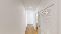 Located at 1172 Republican St in Seattle's South Lake Union neighborhood, this single-floor residence showcases a thoughtfully designed contemporary interior with a clean, minimalist aesthetic. The space is defined by crisp white walls, recessed lighting, and warm hardwood flooring that runs throughout the main living areas.

The standout feature of the living room is a dramatic curved wall of floor-to-ceiling windows that floods the space with abundant natural light and frames views of the surrounding Seattle streetscape. The open-plan layout connects the living area seamlessly to the kitchen, which is outfitted with high-gloss white cabinetry extending to the ceiling, white tile backsplash, light quartz countertops, and a stainless steel range as the culinary centerpiece.

The bedroom is finished with neutral carpet, bright white walls, and a window that brings in natural light, creating a calm, restful environment. A hallway with louvered closet doors and recessed lighting leads to the bathroom, which features light hardwood-style flooring, a white vanity with integrated sink, and a fully tiled walk-in shower with sliding glass doors, maintaining the home's consistent modern character throughout.