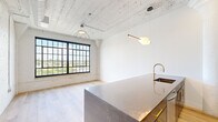 Located at 2528 Texas Ave in St. Louis, Missouri, this thoughtfully renovated loft-style unit showcases a striking blend of industrial character and modern design. Light hardwood flooring flows throughout the single-floor layout, complementing the whitewashed exposed brick walls and raw concrete ceilings that speak to the building's historic roots. Large, multi-pane warehouse-style windows flood the living and bedroom spaces with natural light while offering elevated views of the surrounding neighborhood. The open-concept kitchen features a bold blue island with a stainless steel countertop, gold-accented fixtures, dark cabinetry, stainless steel appliances, and distinctive pendant lighting. A structural column adds an authentic industrial touch to the expansive living area, where exposed ductwork and geometric light fixtures further enhance the loft aesthetic. The bedrooms are bright and versatile, with one featuring a walk-in closet. The bathrooms are finished with clean, modern design elements including white subway-tiled tub-shower surrounds, matte black fixtures, warm wood floating vanities, and illuminated rounded mirrors. The overall ambiance is airy, refined, and full of character, honoring the building's industrial past while delivering a polished, contemporary living experience.