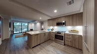 Located at 1825 N Las Palmas Ave in the heart of Hollywood, Los Angeles, this single-floor residence showcases a sleek, contemporary design throughout. The open-concept kitchen is a standout feature, equipped with stainless steel Bosch appliances including a gas range and microwave, flat-panel wood-toned cabinetry, and quartz countertops with a peninsula that doubles as a breakfast bar. Light wood-look flooring flows seamlessly throughout the common areas and bedrooms, reinforcing the modern aesthetic. The living area benefits from floor-to-ceiling sliding glass doors that open directly to a private outdoor patio, bringing in natural light and creating a seamless indoor-outdoor connection with views of lush tropical foliage. The primary bedroom is generously proportioned with a large window overlooking the patio, a wall-mounted TV, and access to a walk-in closet. A second bedroom offers similar comfort and garden views. The bathrooms are finished to a high standard, with the primary bath featuring marble-clad walk-in shower walls, large-format slate-toned floor tiles, a deep soaking tub, and warm wood vanity cabinetry. The overall ambiance of the space is clean, bright, and well-appointed, reflecting a refined urban lifestyle in a premier Los Angeles location.