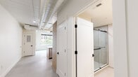 Located at 239 Main St in New Britain, CT, this single-floor unit offers a thoughtfully designed open-concept layout that maximizes its compact footprint. The space features an industrial-modern aesthetic, highlighted by exposed ductwork along the ceiling and polished concrete floors that run throughout. A large window in the living area floods the space with natural light while framing views of the surrounding urban streetscape.

The kitchen is a standout feature, outfitted with light wood cabinetry, a generous peninsula with a gray quartz countertop, and a matte black faucet over an undermount sink. Stainless steel appliances, including a refrigerator, microwave, and range, are integrated seamlessly into the cabinetry. Pendant lights with glass globe shades hang above the peninsula, adding warmth to the otherwise clean, minimal palette.

The bathroom continues the modern design language with a floating wood vanity, a white countertop with an undermount sink, matte black fixtures, a large wall mirror with integrated lighting, and a glass-enclosed shower. White shaker-style interior doors with black hardware provide a cohesive finishing detail throughout. The overall ambiance is clean, contemporary, and efficiently organized.