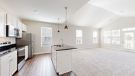 Located at 6650 Liberty Grand Blvd in Powell, Ohio, this single-floor, 3-bedroom, 2-bathroom home offers a thoughtfully designed layout ideal for comfortable everyday living. The open-concept kitchen and living area serves as the heart of the home, featuring a central island with a dark granite countertop, undermount sink, and stylish pendant lighting. White cabinetry, stainless steel appliances, and wood-look flooring complete the kitchen, which flows seamlessly into the carpeted living area bathed in natural light from multiple windows. The primary bedroom is generously sized, with three windows providing abundant natural light and neighborhood views, accompanied by an en suite bathroom finished with dark granite countertops, white cabinetry, and hardwood-style flooring, plus a spacious walk-in closet with wire shelving. The two additional bedrooms are well-proportioned, carpeted, and each feature a ceiling fan or natural light from windows with outdoor views. A dedicated laundry room with wire shelving and appliance hookups adds everyday convenience. Throughout the home, a neutral color palette, clean white trim, and consistent finishes create a bright, cohesive ambiance.