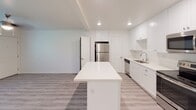 Located at 8155 Cargill in San Diego, this single-floor unit presents a clean, modern aesthetic throughout, highlighted by light wood-style flooring and a crisp all-white color palette. Recessed lighting illuminates each space, enhancing the bright, open atmosphere.

The kitchen is a standout feature, showcasing floor-to-ceiling white shaker cabinets that provide generous storage. A large center island with a quartz countertop serves as a functional focal point, complemented by matching quartz surfaces along the perimeter. Stainless steel appliances, including a range, over-the-range microwave, dishwasher, and full-size refrigerator, complete the well-equipped space.

The bedroom offers a comfortable, airy environment with a ceiling fan, natural light from a window with exterior greenery views, and consistent light wood-style flooring that flows throughout the unit.

The bathroom is finished to a high standard, featuring a white vanity with quartz countertop, a wall-mounted towel bar, and a spacious walk-in shower enclosed by a frameless sliding glass door with subway tile surround and chrome hardware, all set against a clean, white backdrop.
