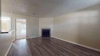 This single-story residence offers a well-organized layout with distinct living areas connected by consistent design elements throughout. The main living area features dark hardwood-style flooring, neutral beige walls, and a textured ceiling. A tiled fireplace with a white mantel serves as a focal point, while a doorway provides a view into an adjacent room with access to the outdoors through a large sliding glass door, allowing natural light to filter in.

A second carpeted room, equipped with a ceiling fan and a sliding glass door overlooking lush greenery, provides a comfortable, light-filled space. The galley-style kitchen is well-equipped with rich wood cabinetry, granite-style countertops, black appliances including a range, microwave, and refrigerator, and light hardwood-style flooring that continues into the connecting hallway.

The bedroom is generously sized with plush carpet, a ceiling fan, and access to both a walk-in closet and an adjoining bathroom. The bathroom features a wood-toned vanity with a granite-style countertop and a vessel sink, complemented by light hardwood-style flooring. The entry area includes dark flooring, a bright window, and a pass-through counter connecting to the kitchen, creating a cohesive and functional flow throughout the space.