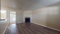 This single-story residence offers a well-organized layout with distinct living areas connected by consistent design elements throughout. The main living area features dark hardwood-style flooring, neutral beige walls, and a textured ceiling. A tiled fireplace with a white mantel serves as a focal point, while a doorway provides a view into an adjacent room with access to the outdoors through a large sliding glass door, allowing natural light to filter in.

A second carpeted room, equipped with a ceiling fan and a sliding glass door overlooking lush greenery, provides a comfortable, light-filled space. The galley-style kitchen is well-equipped with rich wood cabinetry, granite-style countertops, black appliances including a range, microwave, and refrigerator, and light hardwood-style flooring that continues into the connecting hallway.

The bedroom is generously sized with plush carpet, a ceiling fan, and access to both a walk-in closet and an adjoining bathroom. The bathroom features a wood-toned vanity with a granite-style countertop and a vessel sink, complemented by light hardwood-style flooring. The entry area includes dark flooring, a bright window, and a pass-through counter connecting to the kitchen, creating a cohesive and functional flow throughout the space.