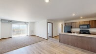 Located at 2109 E Anamosa St in Rapid City, South Dakota, this single-floor, 3-bedroom, 2-bathroom residence offers a well-designed layout with a clean, modern aesthetic. The open-concept living and kitchen area serves as the heart of the home, where light wood-tone laminate flooring flows throughout. The kitchen is equipped with dark wood cabinetry, black appliances including a refrigerator, range, and microwave, and features a peninsula with a built-in sink and light countertops — providing ample prep and storage space. A dishwasher is also included. The living area transitions seamlessly from the kitchen, with a section of plush carpet adding warmth, and access to a private balcony offering sweeping views of the surrounding Rapid City landscape. Each of the three bedrooms features soft carpeting, natural light through blinded windows, and views of the outdoors. The primary bedroom includes sliding glass door access to the balcony. Three closets provide generous storage throughout. Both bathrooms are finished with hexagonal tile flooring in a marble-style pattern and dark wood vanities with light countertops. One bathroom includes a full tub-shower combo. The entry foyer features the same light wood flooring, providing a bright and welcoming introduction to the home.
