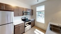 Located at 333 Nord Ave in Chico, California, this single-story unit offers a thoughtfully designed layout with contemporary finishes throughout. The kitchen serves as a central highlight, featuring rich dark wood cabinetry, white countertops, and a full suite of stainless steel appliances including an electric range and built-in microwave. A peninsula with an integrated sink extends the workspace and provides a natural division between the kitchen and the adjacent living area. Pendant lighting hangs above the peninsula, complementing the track lighting overhead, while multiple windows allow generous natural light to fill the space. The living area continues the bright, airy feel with light flooring and a row of windows that bring in additional daylight and outdoor views. Bedrooms are finished with plush carpet, ceiling fans, and wall-mounted mini-split units for individual climate control. The bathrooms are clean and functional, each featuring a tub-shower combination, dark wood cabinetry with granite-style countertops, and light tile flooring. The overall design balances practicality with modern aesthetic touches throughout.