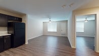This single-floor residence offers a thoughtfully designed open-concept layout that seamlessly connects the kitchen, dining, and living areas. The kitchen is a standout feature, outfitted with rich dark cabinetry, light granite-style countertops, black appliances including a range, microwave, refrigerator, and dishwasher, and durable wood-look flooring. A round dining table with upholstered chairs sits adjacent to the kitchen, providing an inviting space for meals. The living room extends naturally from the dining area, featuring a ceiling fan, neutral tones, and a cozy arrangement anchored by a plush sofa and warm accent pieces. The bedrooms are comfortably sized, each featuring wood-look or hardwood-style flooring, ceiling fans, and windows fitted with blinds that allow for natural light while maintaining privacy. The neutral wall tones and clean lines give the bedrooms a calm, restful ambiance. The bathroom is finished with tile flooring, a dark vanity with a light countertop, and includes accessibility-friendly grab bars near the toilet. Throughout the residence, the consistent use of neutral palettes, modern fixtures, and quality flooring materials creates a cohesive, contemporary aesthetic that is both functional and welcoming.