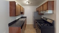 This upgraded single-floor unit offers a well-considered layout designed for comfortable everyday living. The entry area welcomes residents through a bold six-panel door flanked by a large multi-pane window that frames outdoor greenery, with tile flooring transitioning into carpeted living areas.

The open living area is generously proportioned, finished with neutral carpet and a ceiling fan, and flows directly into the galley-style kitchen. The kitchen is equipped with warm wood cabinetry, dark granite countertops, a stainless steel refrigerator, a gas range, and a built-in dishwasher—all arranged efficiently along parallel walls with tile flooring underfoot.

The bedroom is a quiet, carpeted space filled with natural light from a window overlooking the outdoors. The full bathroom mirrors the kitchen's upgraded aesthetic, featuring a dark granite vanity top and wood cabinetry, with tile flooring throughout.

A dedicated laundry room houses a full-size side-by-side washer and dryer, adding everyday convenience. Clean white walls and consistent finishes throughout give the unit a cohesive, move-in-ready feel.