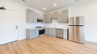 Located at 660 Joseph Ave in Nashville, TN, this efficiently designed one-bedroom, one-bathroom unit offers a clean, modern aesthetic throughout its single floor of living space. The open kitchen is outfitted with gray flat-front cabinetry, white quartz-style countertops, a subway tile backsplash, and a full suite of stainless steel appliances including a gas range, microwave, dishwasher, and refrigerator — all illuminated by recessed lighting and warm wood-tone flooring that carries throughout the unit. The bedroom is a bright, comfortable retreat featuring a ceiling fan, a natural light-admitting window with views of the surrounding neighborhood, and generous closet space including a double-door closet for ample storage. The bathroom is thoughtfully appointed with a gray vanity, white countertop, large mirror with matte black fixtures, a soaking tub and shower combination with white tile surround, and matching wood-look flooring for a cohesive finish. A hallway connects the living spaces cleanly. The unit also features a private balcony enclosed by a sleek navy metal railing, offering open views of Nashville's developing urban landscape. Throughout the unit, crisp white walls, matte black hardware accents, and light hardwood flooring create a cohesive, contemporary atmosphere.
