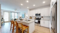 This single-story, one-bedroom, one-bathroom unit offers a thoughtfully designed layout that maximizes its compact footprint. The open-concept kitchen and living area serve as the heart of the space, where light-toned, wood-look flooring flows continuously underfoot. The kitchen is outfitted with crisp white cabinetry, a subway tile backsplash, granite countertops, and a full suite of stainless steel appliances including a range, microwave, and refrigerator. A peninsula with seating provides a casual dining option while maintaining visual continuity with the adjacent living room.

The living room benefits from large windows and a glass door that invite natural light and feature a ceiling fan overhead. The bedroom, carpeted for comfort, accommodates a generous furniture arrangement and is served by a dedicated walk-in closet with wire shelving systems offering organized storage. The bathroom includes a tub-shower combination with white subway tile surround, a granite-topped vanity with white cabinetry, and wood-look flooring. The unit is situated within a well-landscaped residential community featuring manicured grounds and surface parking.