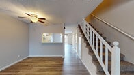 This two-story home is designed for comfortable everyday living, with a thoughtful layout that separates common areas from private spaces across two distinct levels. The main floor opens into a spacious living area finished with wood-look laminate flooring and a ceiling fan, creating a bright and airy atmosphere. A sliding glass door at the rear provides direct access to a fenced outdoor area, filling the room with natural light. The kitchen features white cabinetry, a tile backsplash, a double-basin sink, and white appliances including a range, built-in microwave, refrigerator, and dishwasher. A pass-through window connects the kitchen to the living space, enhancing the open feel of the main level. A carpeted staircase with a white balustrade leads to the upper floor, where the bedrooms are located. The primary bedroom is generously sized with plush carpet, a ceiling fan, a sliding glass door opening to a private balcony, and a walk-in closet. The primary bathroom offers a dual-sink vanity with tile backsplash, wood-look flooring, and ample storage. Additional bedrooms on the upper level are carpeted and naturally lit through windows with blinds. Textured ceilings and neutral tones throughout give the home a clean, cohesive look.