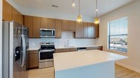 Located at 1341 Norton Ave in Columbus, Ohio's Grandview Heights area, this single-floor residence offers a thoughtfully designed layout with modern finishes throughout. The kitchen is a standout feature, showcasing warm walnut-toned cabinetry, quartz countertops, a large center island, and a full suite of stainless steel appliances including a refrigerator with ice maker, electric range, built-in microwave, and dishwasher. A textured chevron-pattern tile backsplash adds visual interest, while pendant lighting above the island and recessed ceiling lights create a warm, functional ambiance. Light hardwood-style flooring extends from the kitchen into the open living area, which benefits from natural light through a window with exterior views. A separate room with the same light flooring features a built-in shelf, offering flexibility as a bedroom or office space. The primary bedroom is carpeted and includes a generously sized walk-in closet with wire shelving and dual sliding panel doors. The bathroom is finished in a clean, contemporary style with wood-toned cabinetry, quartz countertops, light tile flooring, and a tiled walk-in shower. Throughout the space, a neutral color palette and consistent modern design elements create a cohesive and inviting atmosphere.