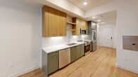 Located at 222 N West St in downtown Raleigh, NC, this thoughtfully designed one-bedroom, one-bathroom unit offers a modern and efficient layout across a single floor. Light-toned hardwood flooring flows throughout, creating a cohesive and welcoming ambiance.

The galley-style kitchen is a standout feature, showcasing sage green lower cabinets paired with warm wood-toned upper cabinetry and open shelving. A herringbone tile backsplash, white quartz countertops, and a full suite of stainless steel appliances — including a French door refrigerator, electric range, over-the-range microwave, and dishwasher — complete this well-appointed space.

The living area benefits from recessed lighting and an open feel that leads naturally to the bedroom. The bedroom is bright and comfortable, featuring a large window with outdoor views of the surrounding Raleigh streetscape and a ceiling fan for added comfort. Three closets throughout the unit provide generous storage options.

The bathroom offers a clean, modern aesthetic with white subway tile surrounding a full soaking tub and shower combination, complemented by chrome fixtures, a vanity with a white countertop, and hardwood-style flooring. A dedicated utility room and electrical panel access round out the practical amenities of this well-planned unit.