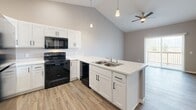Located at 3276 Jim St in Rapid City, South Dakota, this single-floor, 2-bedroom, 1-bathroom home offers a well-designed layout with modern finishes and practical living spaces. The open-concept kitchen is a standout feature, boasting vaulted ceilings that create an airy atmosphere, white shaker cabinetry, light quartz countertops, and a peninsula with a double-basin sink. Black appliances — including a range, microwave, and dishwasher — provide a clean contrast to the bright cabinetry. Pendant lighting and recessed lights illuminate the kitchen, which flows naturally into the living area, where a ceiling fan and access to an outdoor space add comfort and functionality. Both bedrooms are carpeted and finished in neutral tones, each benefiting from natural light through windows with blinds. The primary bedroom offers a generous footprint and dedicated closet space. A hallway connects the rooms efficiently, with two closets providing ample storage throughout. A dedicated in-unit laundry area accommodates a full-size washer and dryer side-by-side with overhead shelving. Wood-look flooring runs through the main living areas, complementing the home's cohesive, contemporary aesthetic. The overall design is clean, functional, and move-in ready.