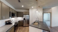 This single-story residence located in Grandover Village, Greensboro, NC, offers a thoughtfully designed layout with contemporary finishes throughout. The open-concept living and kitchen area serves as the heart of the home, featuring rich wood-look flooring, elevated ceilings, recessed lighting, and a ceiling fan. The kitchen is outfitted with taupe shaker-style cabinetry extending to the ceiling for ample storage, stainless steel appliances including a side-by-side refrigerator with ice and water dispenser, a gas range, and a microwave. A peninsula with dark granite countertops and an undermount sink provides additional workspace and casual seating, while two elegant glass pendant lights add a refined touch. White subway tile backsplash completes the modern aesthetic.

The bedrooms feature plush carpeting, ceiling fans, and large windows that invite generous natural light and exterior views. The primary bathroom includes dark wood cabinetry, stone-look countertops, a wide vanity mirror, and tile flooring, with an adjacent walk-in closet. A secondary bathroom offers a tub-shower combination with tiled surround, a framed vanity mirror, and stone-look countertops. The overall ambiance is clean, bright, and modern.