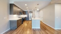 This 660-square-foot, one-bedroom, one-bathroom apartment at 1774 Metro Avenue in Chula Vista, CA offers a well-designed, modern living space across a single floor. The open-concept kitchen and living area is the heart of the unit, featuring dark wood cabinetry with brushed nickel hardware, crisp white quartz countertops, a central island with pendant lighting, and a full suite of stainless steel appliances including a gas range, microwave, and refrigerator. Warm wood-look flooring flows throughout the entire unit, complementing the neutral wall tones. The living area is bright and airy, benefiting from large windows and a glass door that invite abundant natural light and outdoor views of the surrounding community. The 170-square-foot primary bedroom is generously sized with large windows and direct access to a dedicated walk-in closet equipped with built-in shelving and double hanging rods. The bathroom features a dual-sink vanity with navy blue cabinetry, white quartz countertops, a large mirror, and a tiled soaking tub/shower combination. Clean architectural lines and contemporary finishes give this apartment a cohesive, move-in-ready aesthetic ideal for modern living in San Diego County.