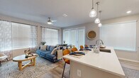 This single-story residence offers a thoughtfully designed open-concept layout that seamlessly connects the kitchen, dining, and living areas into one cohesive, light-filled space. The kitchen is outfitted with white shaker cabinetry reaching toward the ceiling, stainless steel appliances including a side-by-side refrigerator, electric range, and microwave, all complemented by light wood-tone flooring that runs throughout the main living areas. A white waterfall-edge island with pendant lighting above serves as both a functional workspace and a casual dining spot with seating.

The living area is generously proportioned, featuring large windows dressed with layered blinds and sheer curtains that allow ample natural light. A ceiling fan adds comfort, while a sliding glass door connects the dining nook to the outdoors. The space accommodates both a dining table and a full living room arrangement with ease.

Both bedrooms are carpeted and well-lit via large windows, offering a calm retreat. Each includes closet storage, with one bedroom featuring a spacious walk-in closet with wire shelving. The bathroom includes a tub-shower combination, wood-look tile flooring, and a white vanity with ample counter space, completing this well-rounded residence.