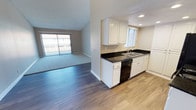 This single-story space showcases a thoughtful open-concept layout that seamlessly connects the kitchen and living areas. The kitchen is well-appointed with crisp white cabinetry extending to the ceiling, striking dark granite countertops, a stainless steel sink, and black appliances including a range, dishwasher, and refrigerator. Recessed lighting illuminates the kitchen, complemented by a window that brings in natural light. Light wood-style flooring runs throughout the kitchen and transitional areas, creating a clean, modern feel.

The living area features vaulted ceilings that enhance the sense of openness, a ceiling fan, and a large sliding glass door that invites natural light and provides outdoor access. Neutral carpet adds warmth underfoot in the living and bedroom spaces. The bedrooms are carpeted and generously proportioned, each benefiting from vaulted or angled ceilings that add architectural interest. Both bedrooms include mirrored sliding closet doors, maximizing storage while reflecting light. Neutral warm-toned walls and textured ceilings are consistent throughout, contributing to a cohesive and inviting overall ambiance.