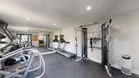 Located at 2550 E Riverside Dr in Ontario, California, this fitness center offers a well-organized exercise space designed to support a variety of workout routines. The room features durable dark flooring throughout and is illuminated by recessed ceiling lighting, creating a bright and functional environment. A full-length wall mirror visually expands the space and allows users to monitor their form during exercise.

The facility is equipped with an array of cardio machines, including multiple treadmills, an elliptical trainer, and a stationary Stages spin bike. A Matrix cable machine with multiple attachment options provides versatile strength training capabilities, while a dedicated weight rack stocked with a range of dumbbells supports free-weight exercises. An adjustable weight bench is also available for targeted strength work.

A wall-mounted flat-screen television adds an entertainment element to workouts. Climate comfort is maintained by a wall-mounted mini-split air conditioning unit, ensuring a pleasant exercise environment year-round. Natural light enters through windows, and a glass-panel entry door connects the space to the exterior. Fitness center rules are clearly posted near the entrance. The overall design is clean, modern, and efficiently laid out to maximize usability within its compact footprint.