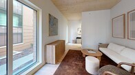 Located on West Main Street in the heart of downtown Madison, Wisconsin, this thoughtfully designed 2-bedroom, 2-bathroom residence showcases a refined modern aesthetic across its single floor. A distinctive natural wood-planked ceiling spans the living and kitchen areas, lending warmth and architectural character to the open-concept layout. Large floor-to-ceiling windows flood the space with natural light while framing views of the surrounding streetscape.

The living area offers a comfortable, understated ambiance with light hardwood flooring, clean white walls, and ample room for relaxed seating arrangements. It flows seamlessly into the kitchen, which is outfitted with sleek flat-front cabinetry in a muted grey finish, stainless steel appliances, under-cabinet lighting, and a generous island ideal for dining or meal prep.

The primary bedroom is a serene retreat, featuring the same warm wood ceiling, soft carpeting, and a large window with outdoor access. The second bedroom is equally well-appointed with access to natural light and a dedicated closet. Both bathrooms are finished with large-format tile, terrazzo-style stone sinks, and modern fixtures — one featuring a walk-in glass-enclosed shower, the other a full soaking tub with tiled surround. A connecting hallway ties all rooms together efficiently.