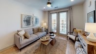 This thoughtfully designed single-floor residence offers a seamless blend of modern finishes and comfortable living. The entryway opens directly into a well-equipped kitchen featuring white shaker-style cabinetry, quartz countertops, a geometric tile backsplash, and a full suite of stainless steel appliances. Light wood-style flooring flows throughout the main living areas, adding warmth and continuity to the space.

The living room is bright and inviting, anchored by large glass doors that open to a private balcony, allowing natural light to fill the room. A ceiling fan overhead adds to the comfort of the space, while the open layout creates an easy connection between living and dining areas.

The bedroom is a restful retreat, featuring plush carpeting, large windows dressed with elegant curtains that invite in natural light, and ample space for a full furniture arrangement including a work desk area.

The bathroom is clean and contemporary, showcasing a wide vanity with white cabinetry, quartz countertops, and a large mirror illuminated by modern fixtures. Wood-style flooring continues here, and a walk-in closet with built-in shelving is directly accessible from the bathroom, offering excellent storage and organization. Overall, the residence presents a cohesive, modern aesthetic with functional, high-quality finishes throughout.
