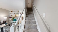 Located at 8600 S Course Dr in Houston, TX, this two-story home offers a thoughtfully arranged layout across two levels. The ground floor welcomes you into a light-filled living room featuring tile flooring, a built-in shelving unit, and large windows that allow natural light to fill the space. A carpeted staircase with white-painted railings leads to the upper level, adding a classic architectural touch. Adjacent to the living area, the dining room accommodates a round wooden table beneath a multi-bulb chandelier, accented by a decorative mirror and wainscoting along the walls. The galley-style kitchen is equipped with rich dark wood cabinetry, granite-style countertops, and white appliances, with tile flooring throughout. Upstairs, the generously sized primary bedroom features soft carpet, a ceiling fan, and ample space for a dedicated sitting area. Three bathrooms serve the home, including one with a tiled tub-shower combination. A dedicated closet provides additional storage. The home's neutral color palette and clean finishes create a cohesive, comfortable ambiance throughout both floors.